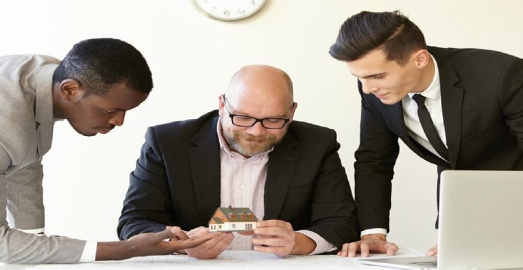 three office men estimating mock up model future terraced house caucasian engineer glasses holding miniature smiling other colleagues suits looking tiny house with interest 273609 5766